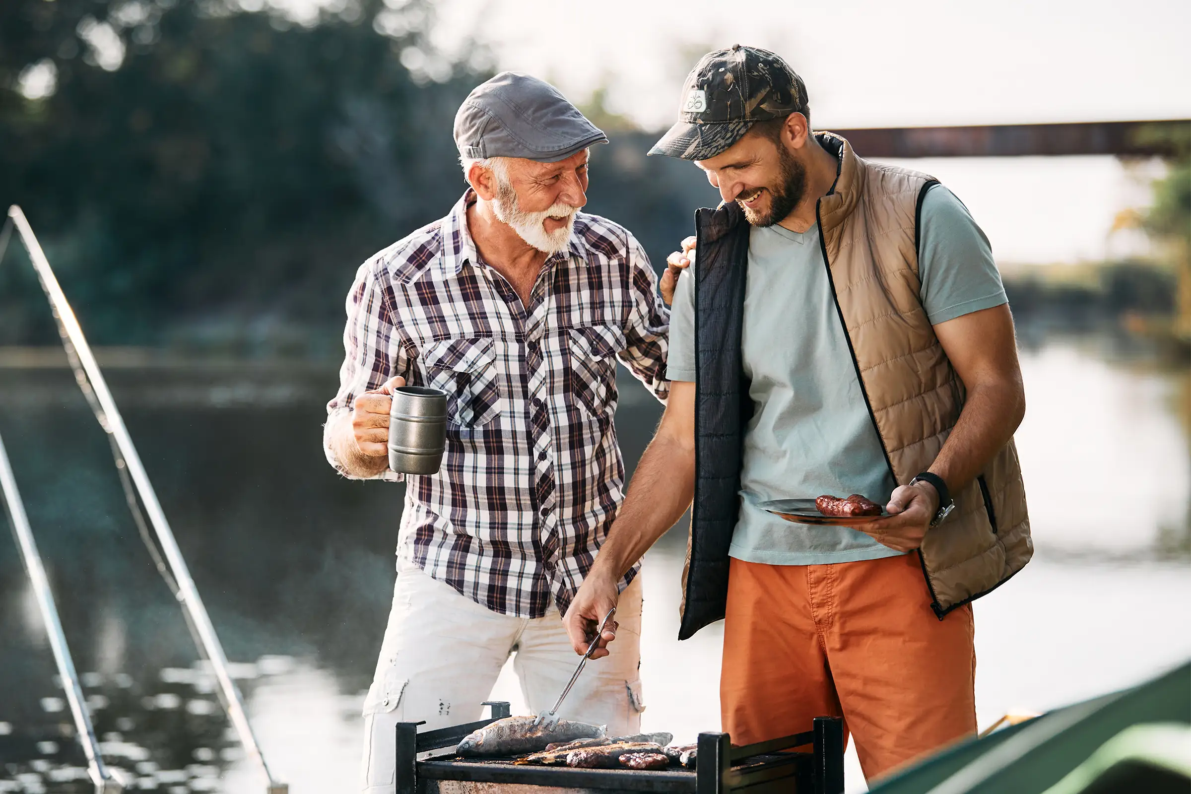 Older and younger man grilling by a lake